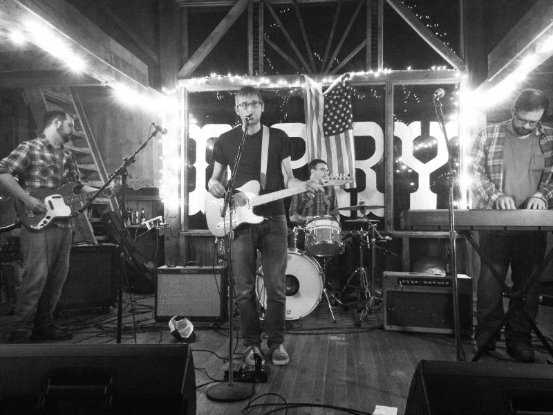 Black and white photo of a band playing onstage in a barn.
