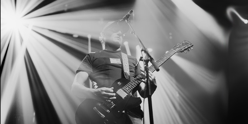A black and white photo of a guitarist performs on a stage performing with all of the spotlights shining all around him.