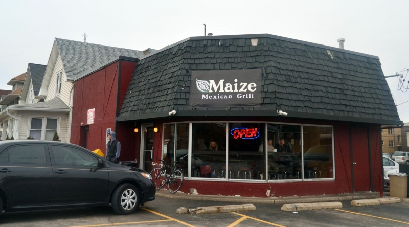 Maize restaurant on Green Street is a small, oddly shaped red building with a black, low hanging roof. There is a sign that says "Maize" over the door. 
