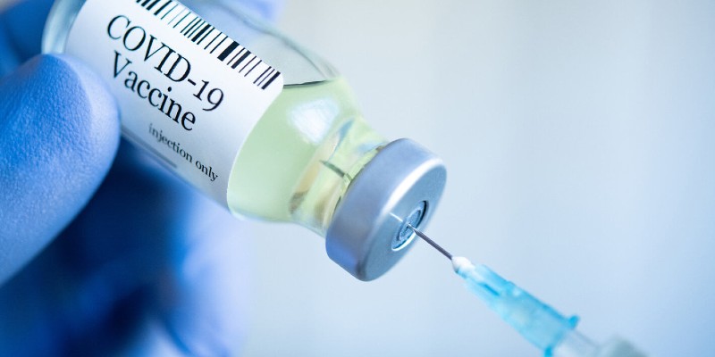 A COVID-19 vaccine vial held by a gloved hand, with a syringe in the top extracting the vaccine.