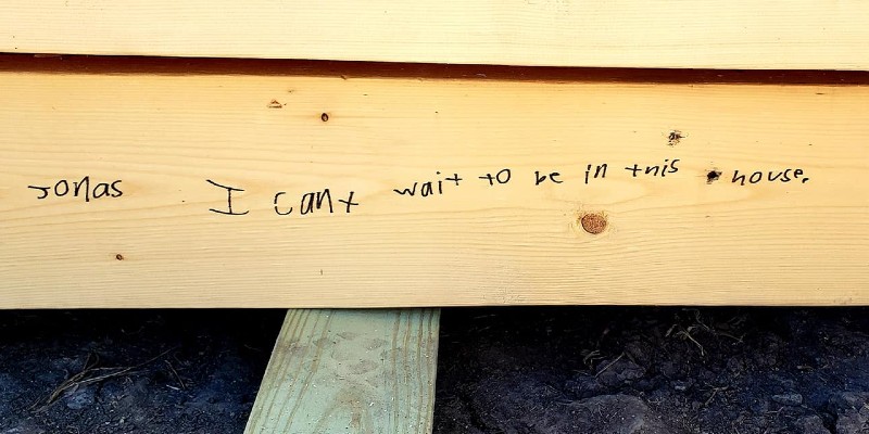 Close up of a wooden beam of a house. It has child's handwriting in black marker that says "I can't wait to be in this house."