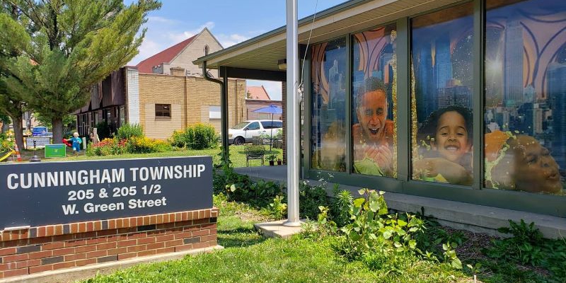 Exterior view of Cunningham Township Office in Urbana. On the right is the building, with a mural by Blackmau. On the left is a dark gray sign with white lettering that says "Cunningham Township" with the address.