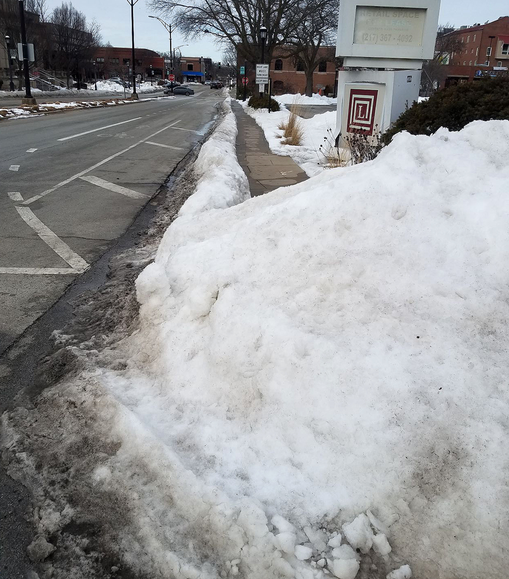 A massive icy snow pile blocks a sidewalk crosswalk in front of Lincoln Square Mall in Urbana. Photo by Deborah Liu. 