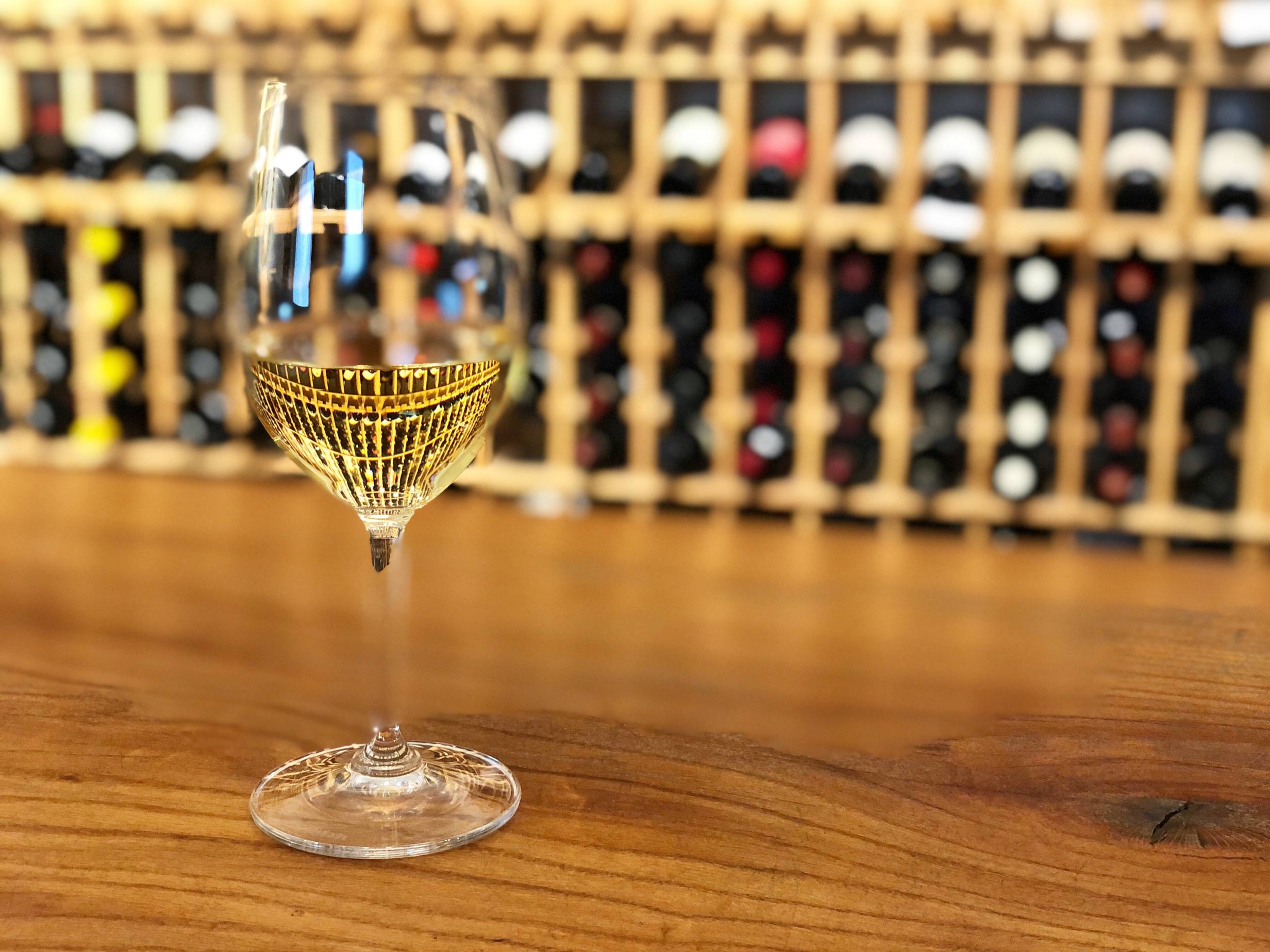 On a wooden bar, there is a single glass of white wine at Art Mart in the wine department. Photo by Alyssa Buckley.