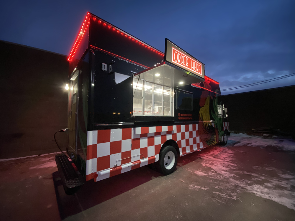 A Watson's food truck painted black with a white and red checked bottom, featuring a walk up window.