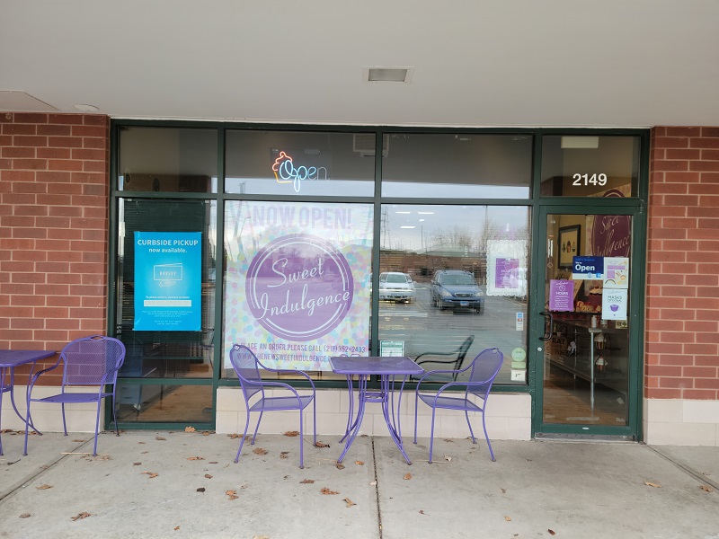The exterior of The New Sweet Indulgence with four purple chairs and two tables close to the door. Photo by Matthew Macomber.