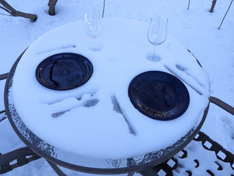 A close up of the snowy table. There are two round black plates, two clear wine glasses, and forks, spoons, and knives alongside each plate. Photo by Tom Ackerman.