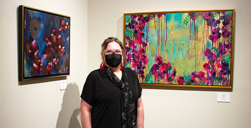 Artist Shannon Percoco standing between two of her floral paintings.