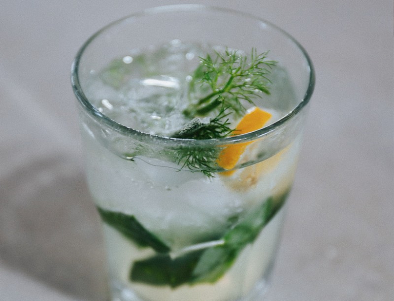 Photo of a cocktail with clear-colored liquid, some green herb garnishes and a lemon wedge. Photo from the Common Ground Food Co-op Facebook page.