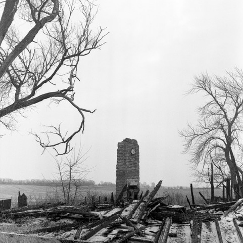 Dust and Ashes by photographer Micah McCoy in black and white shows a bare tree and clocktower rising above the ruins.