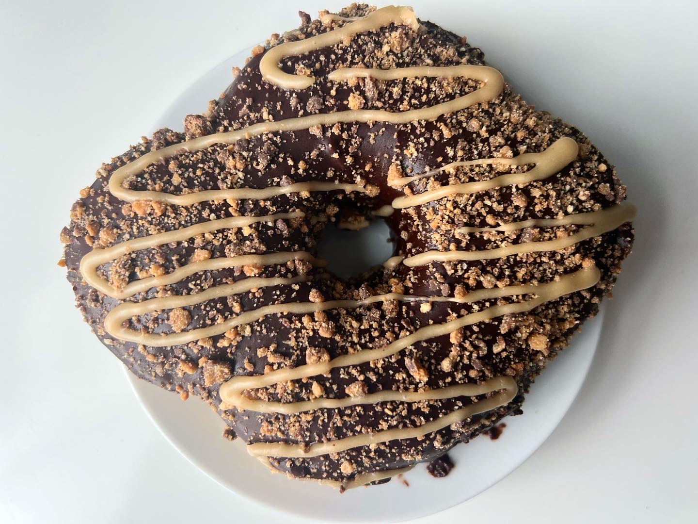 On a white plate, there is a giant chocolate donut with a light brown peanut butter drizzle. Photo by Alyssa Buckley.