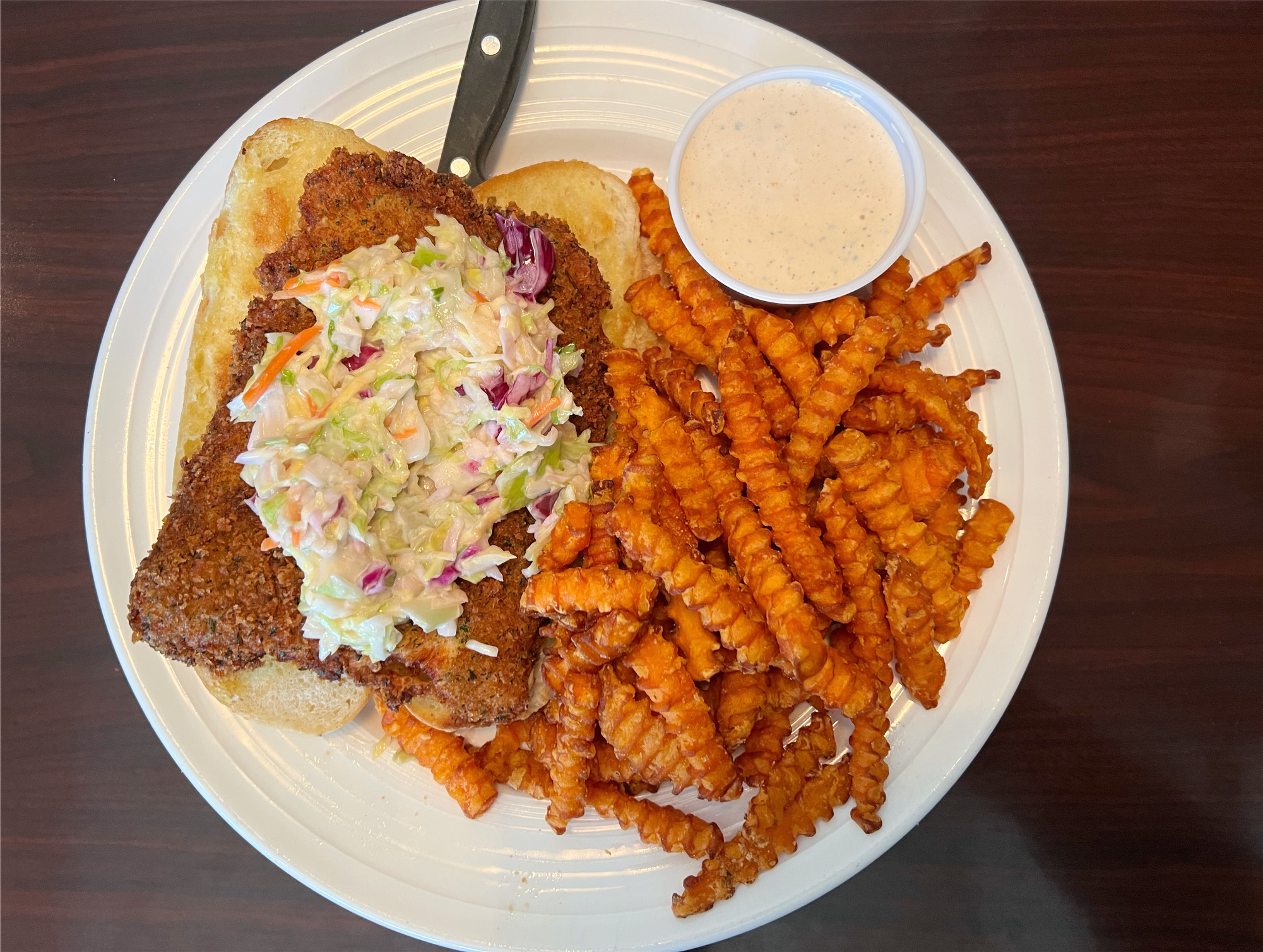 On a white plate, there is a sandwich with a large piece of fried breaded fish with a scoop of creamy coleslaw on top. Photo by Alyssa Buckley.