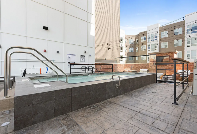 A long rectangular hot tub with dark tiles around the sides and on the surrounding floor. There are several railings around it. Photo by Tom Ackerman.