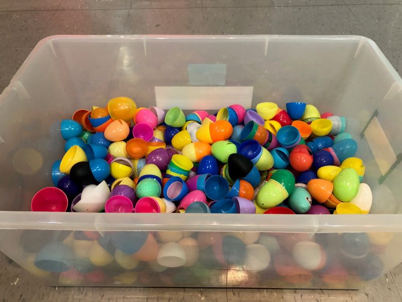 A large rectangular clear plastic tub is filled halfway with an assortment of plastic Easter egg halves. They are all different colors. Photo by Julie McClure.