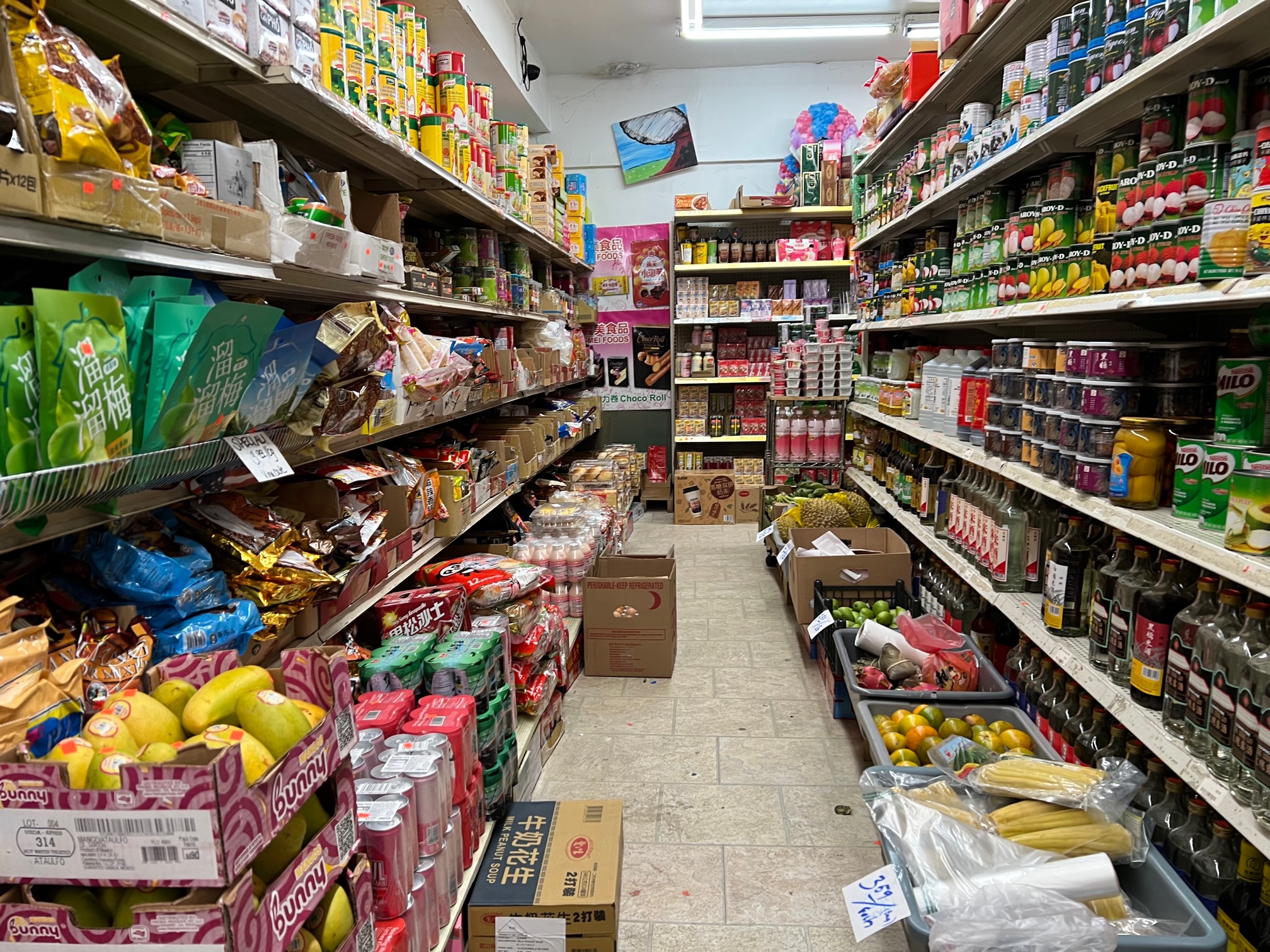 Down one of the aisles at Far East Grocery, there are packages full on the shelves and boxes stacked on top of each other with produce on the ground. Photo by Alyssa Buckley.