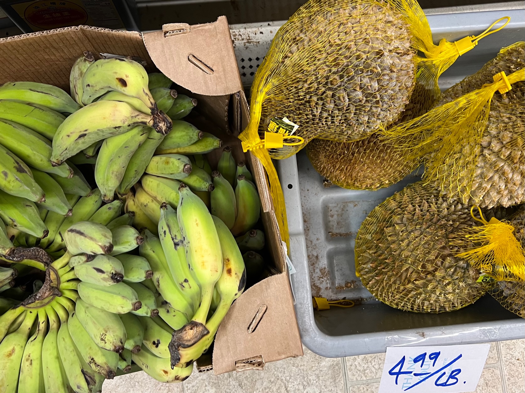 On the floor, there is a large box of bananas in a bunch, and a gray plastic bin of durian fruit. Photo by Alyssa Buckley.