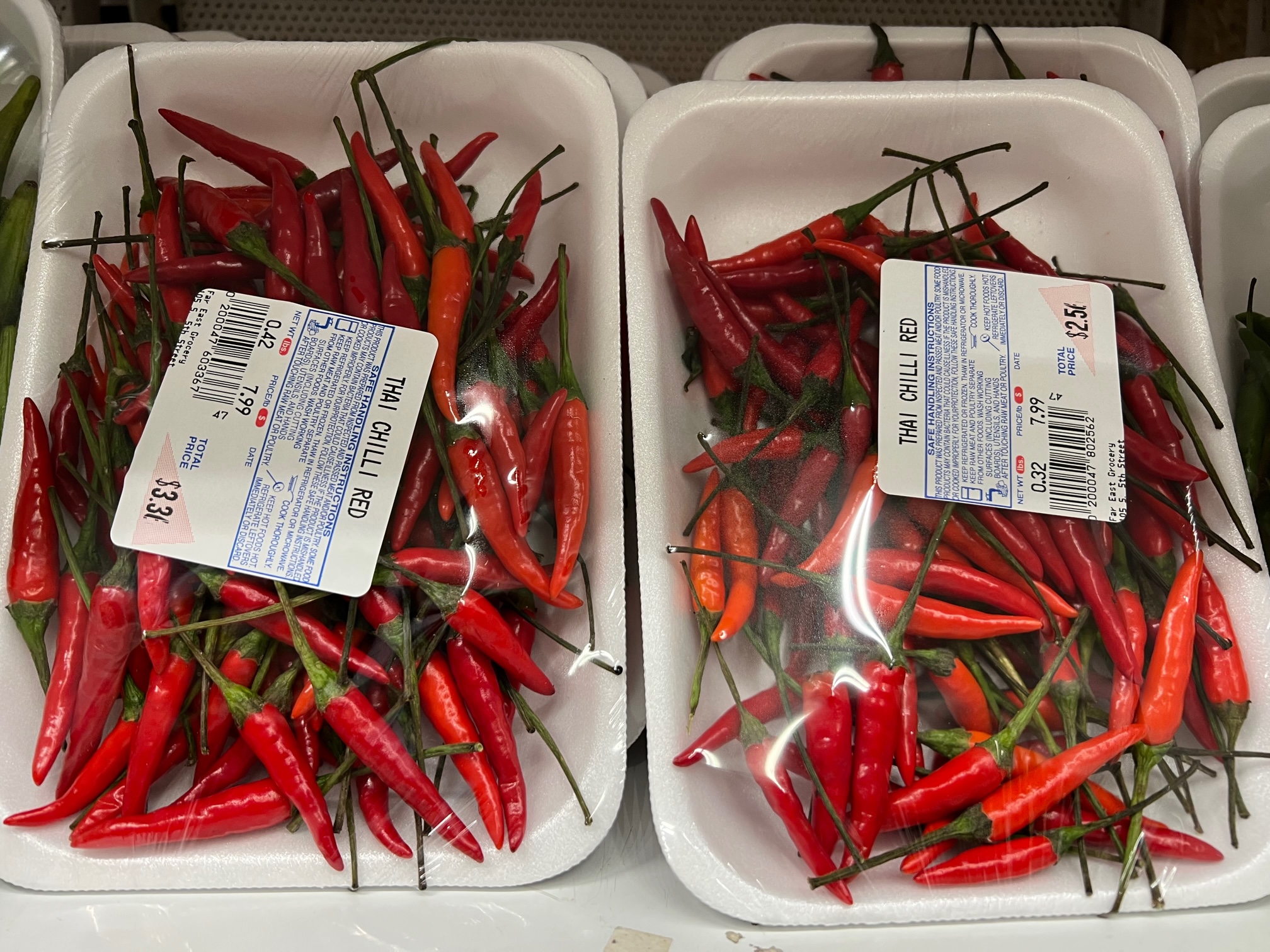 Two packages of tiny Thai chili peppers are standing up tall on the shelf at Far East Grocery. Photo by Alyssa Buckley.