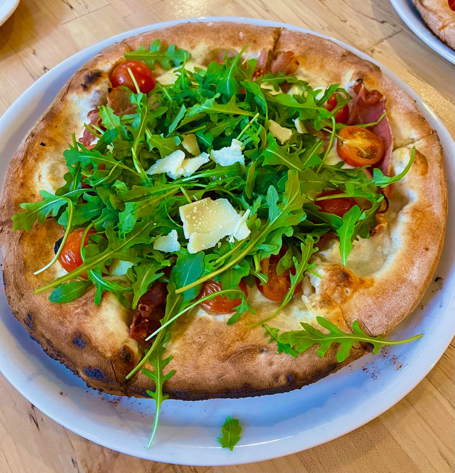 On a white plate, there is a sauceless pizza topped with shaved Parm and lots of arugula. Photo by Stephanie Wheatley.