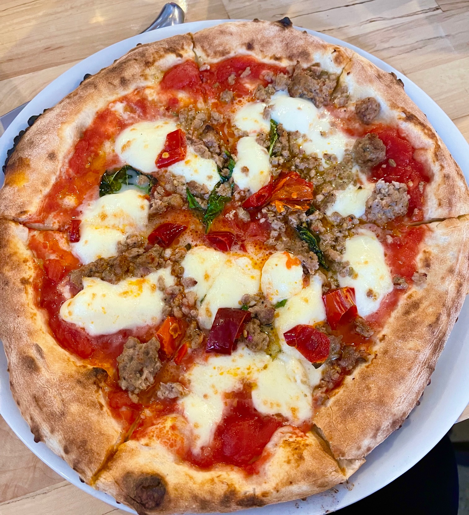 An overhead photo shows a full pie of pizza with crumble sausage, basil, peppers, red sauce, and lots of cheese. Photo by Stephanie Wheatley.