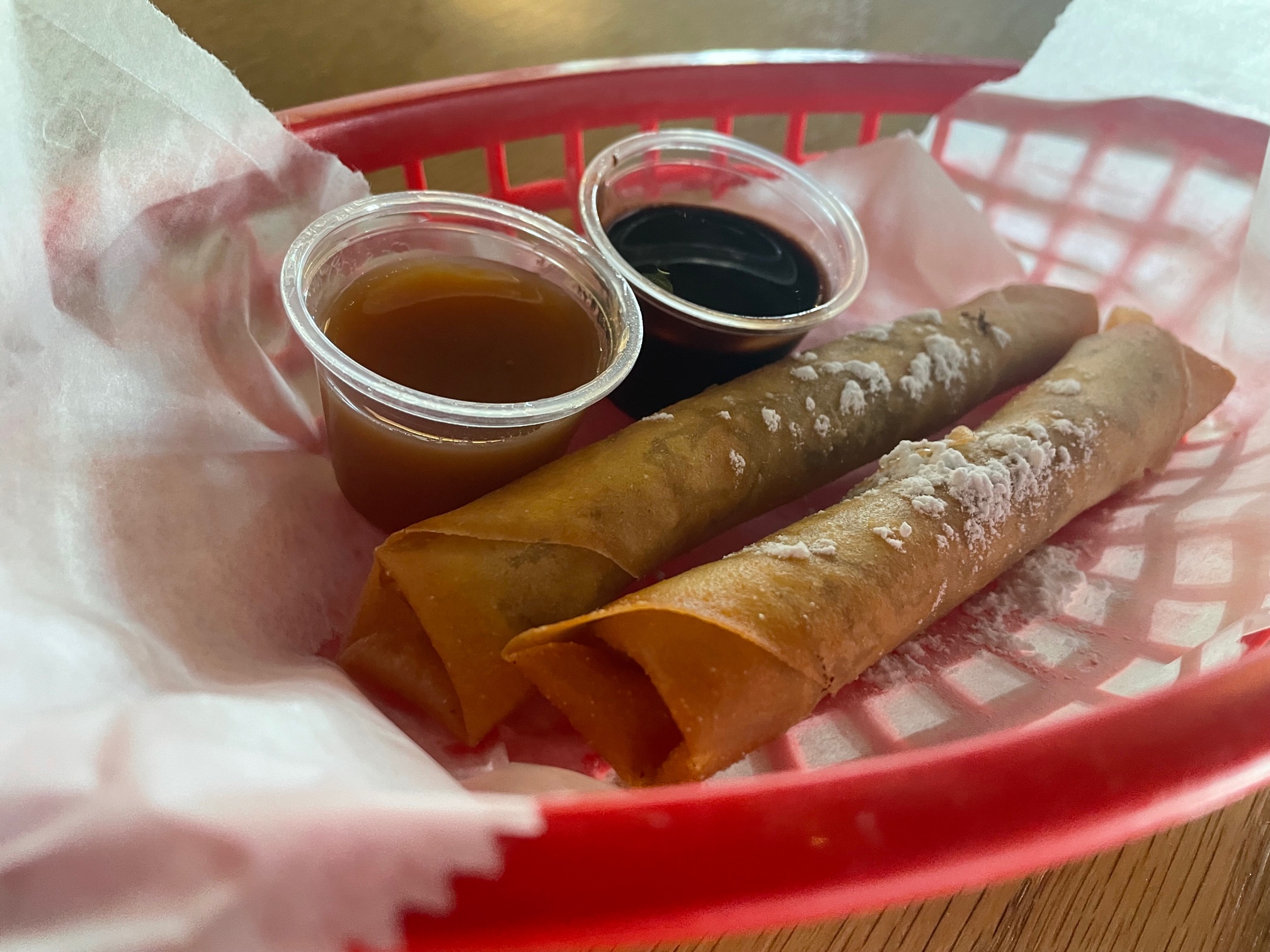 In a red plastic basket lined with parchment paper, there are two turons with two dipping sauces. Photo by Alyssa Buckley.