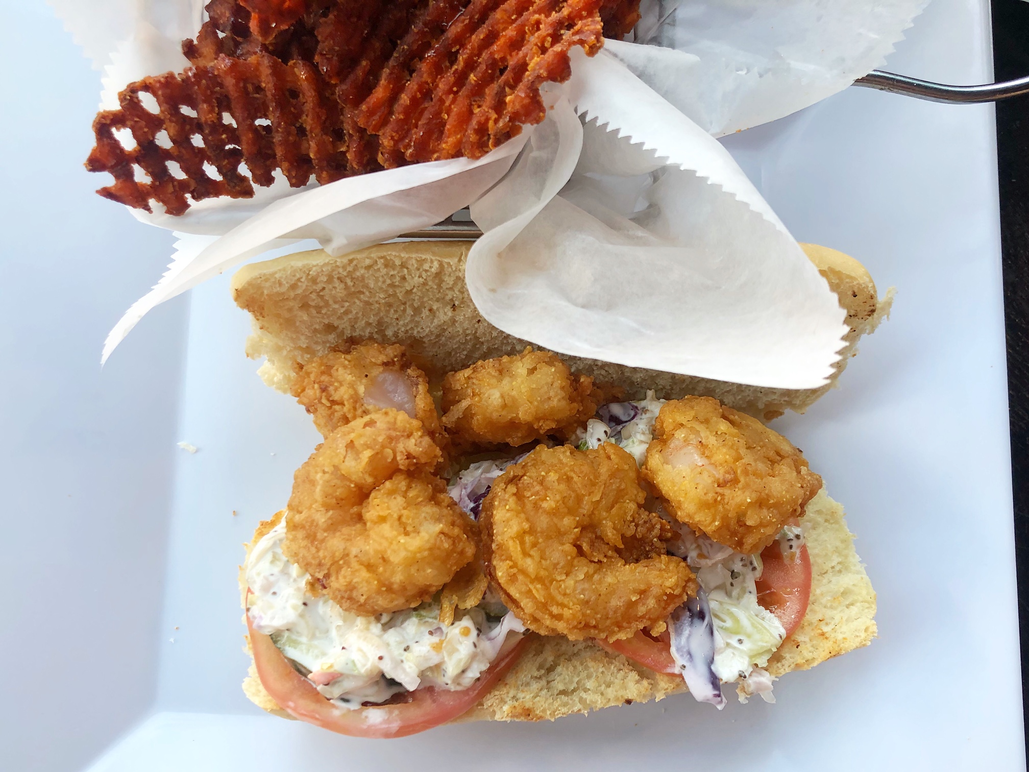 An overhead photo of a po boy from Neil St. Blues shows a several fried shrimp atop coleslaw on a white bun on a white plate. Photo by Alyssa Buckley.