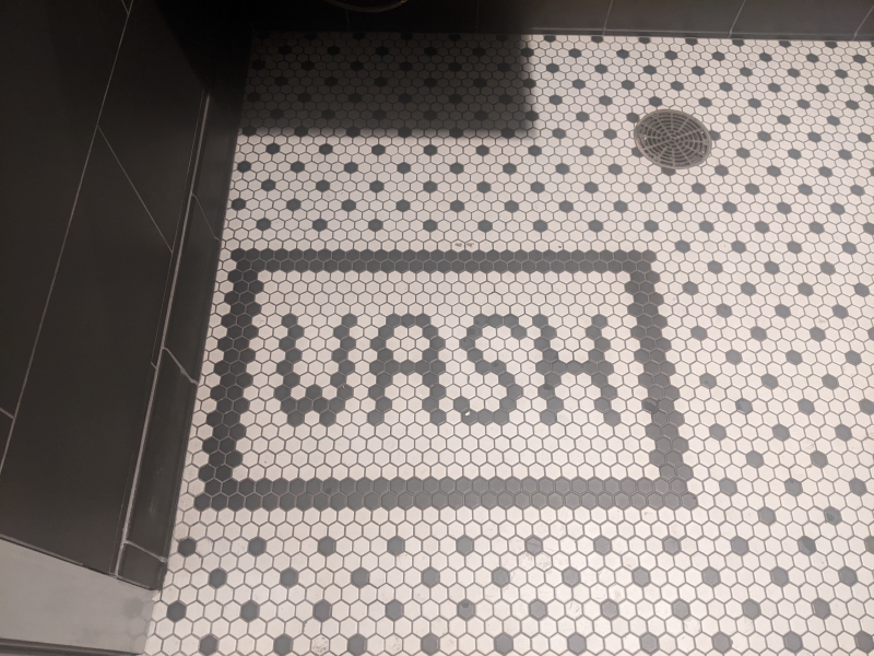 A black and white mosaic tile floor. The word WASH is spelled out in black, with a black rectangle framing it. Photo by Tom Ackerman.