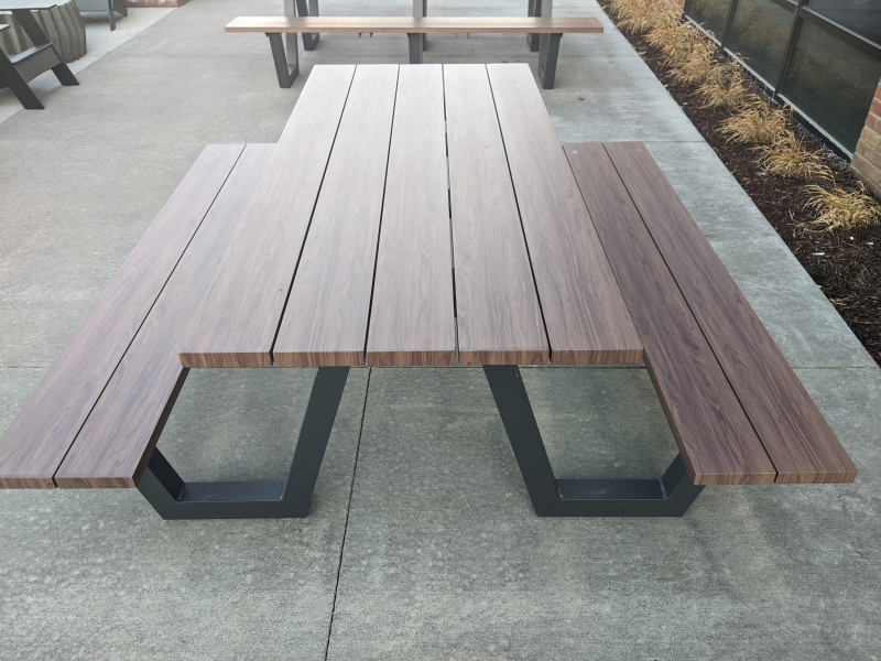 A wooden picnic table with black supports sits on a concrete patio. Photo by Tom Ackerman.