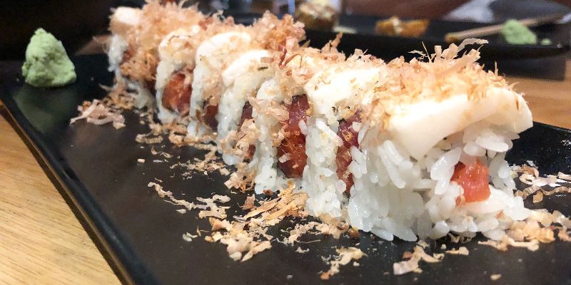 On a rectangular black plate, there is a sushi roll topped with scallops and topped with tempura crunch at Sakanaya in Champaign. Photo by Alyssa Buckley.