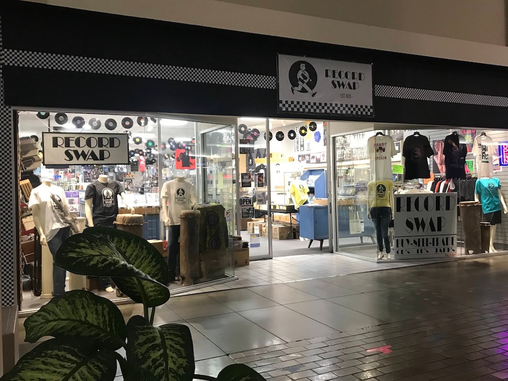 Outside photo of Record Swap in Lincoln Square Mall. There are signs in the window, records hanging all over the store. 
