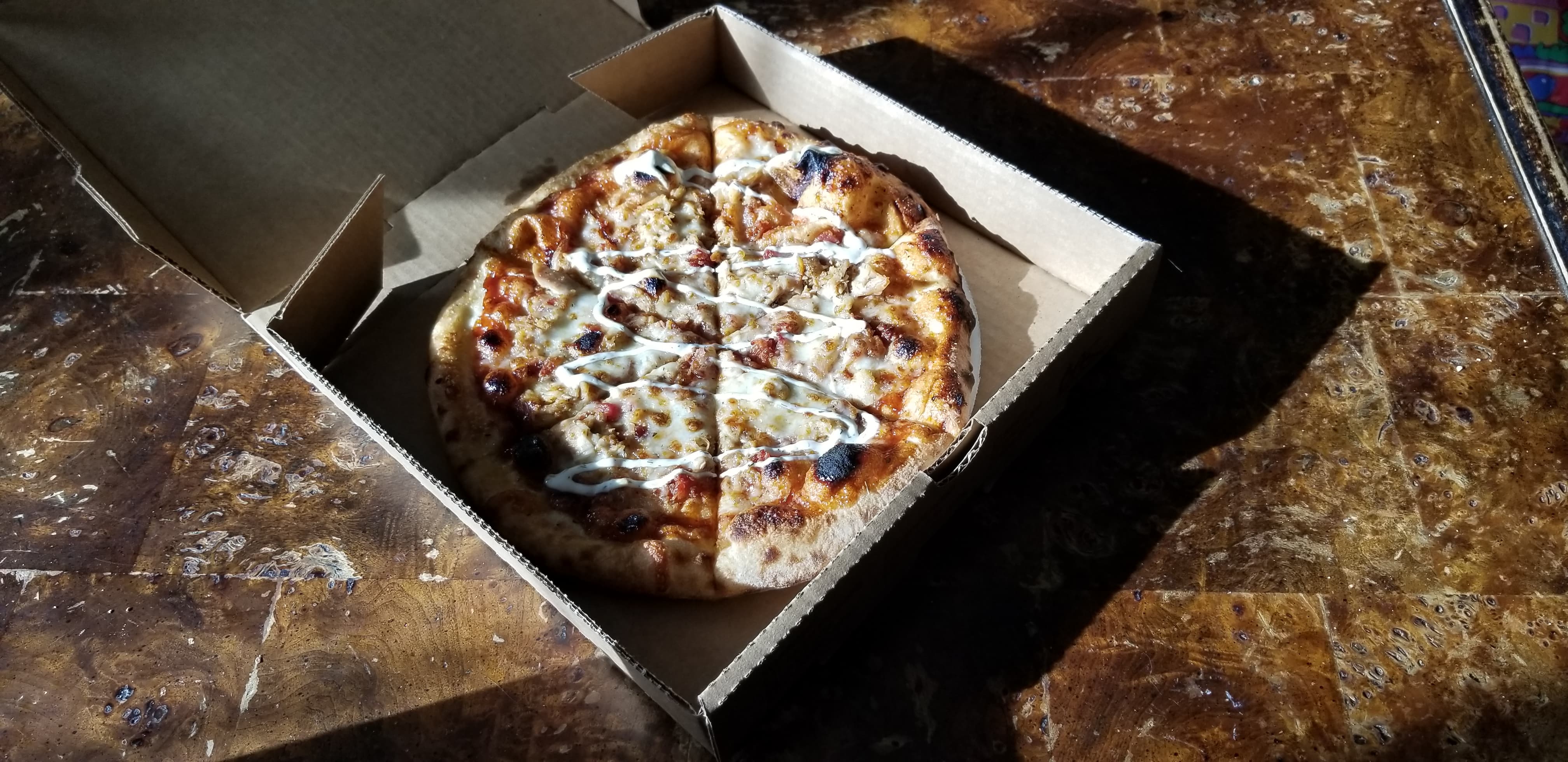 On a sunny table, there is a full pizza pie of BBQ chicken ranch pizza. Photo by Nina Hopkins.