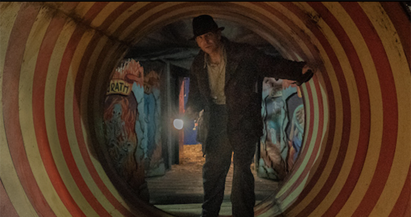 Still shot from Nightmare Alley with actor waling through a brightly colored circus-like tunnel. 