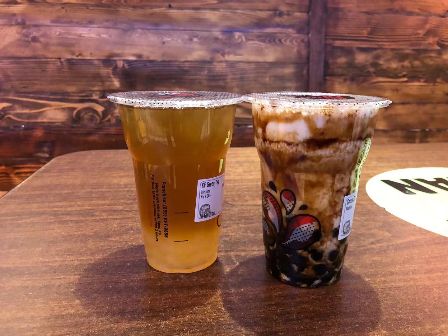 On a brown wooden table, there are two boba drinks in plastic to go cups with covers. Photo by Xiaohui Zhang.
