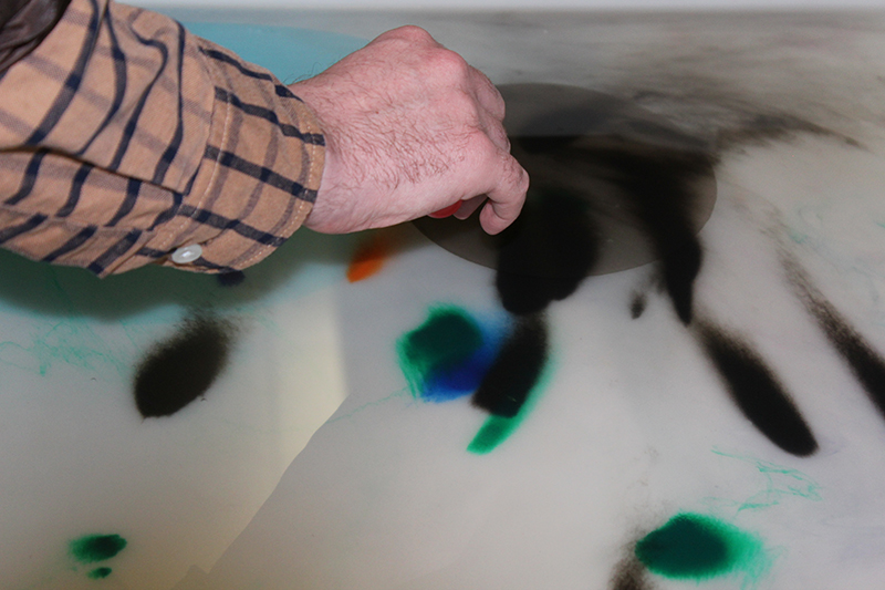 Close up of hand mixing marbling ink in water. 