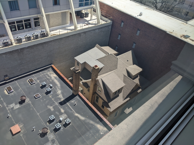 A birds eye view of a house that is nestled behind four larger buildings. Photo by Tom Ackerman.