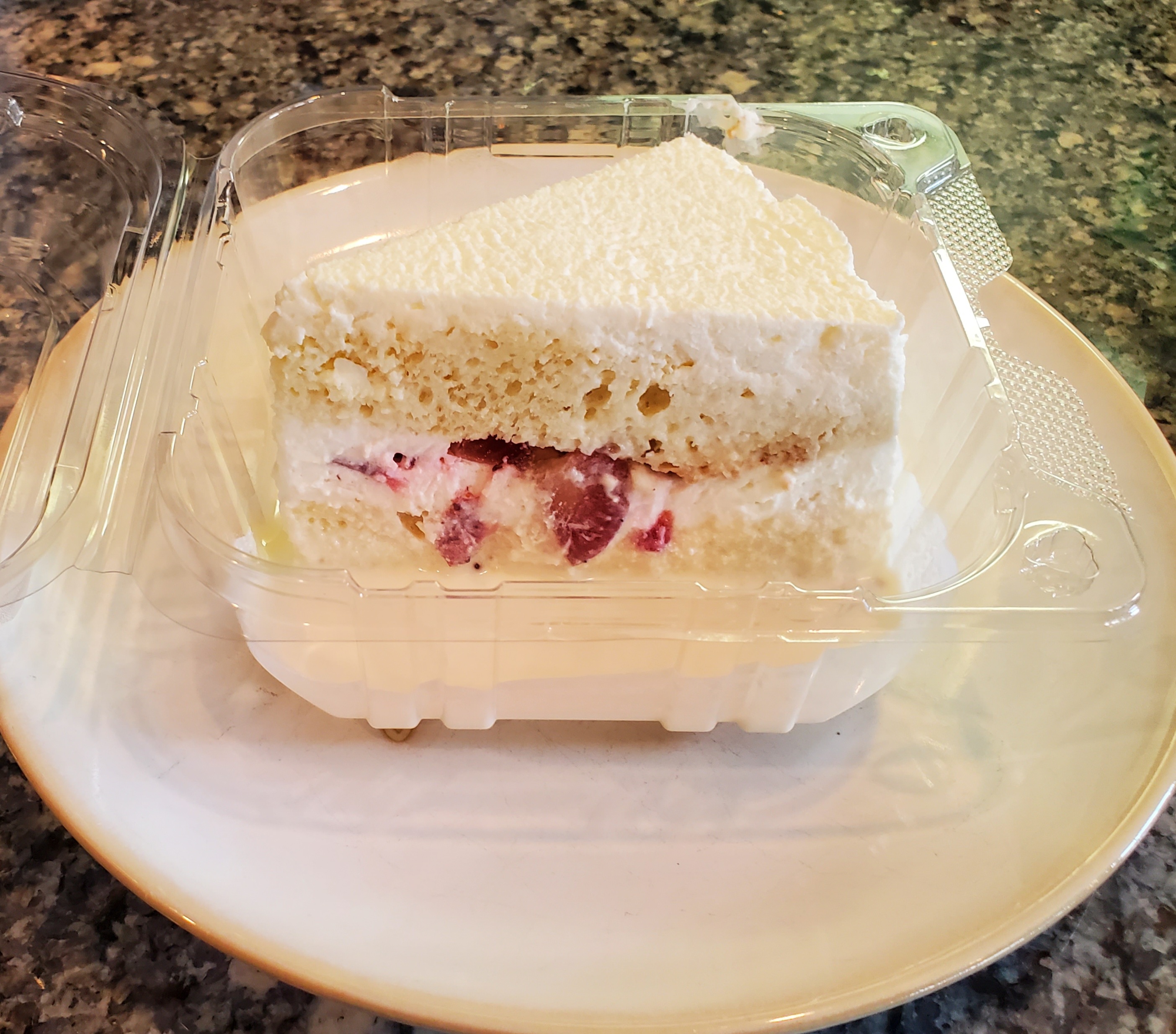 On a white plate, there is a tres leches cake in a plastic clamshell container. Photo by Carl Busch.