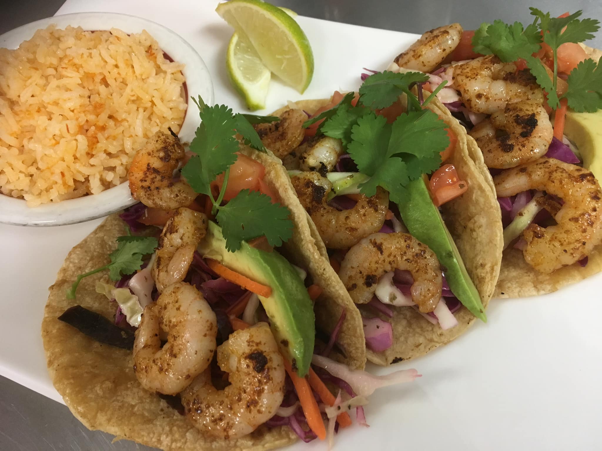 On a white plate, there are three shrimp tacos with a side of rice and two lime wedges. Photo by La Mixteca's Facebook page.