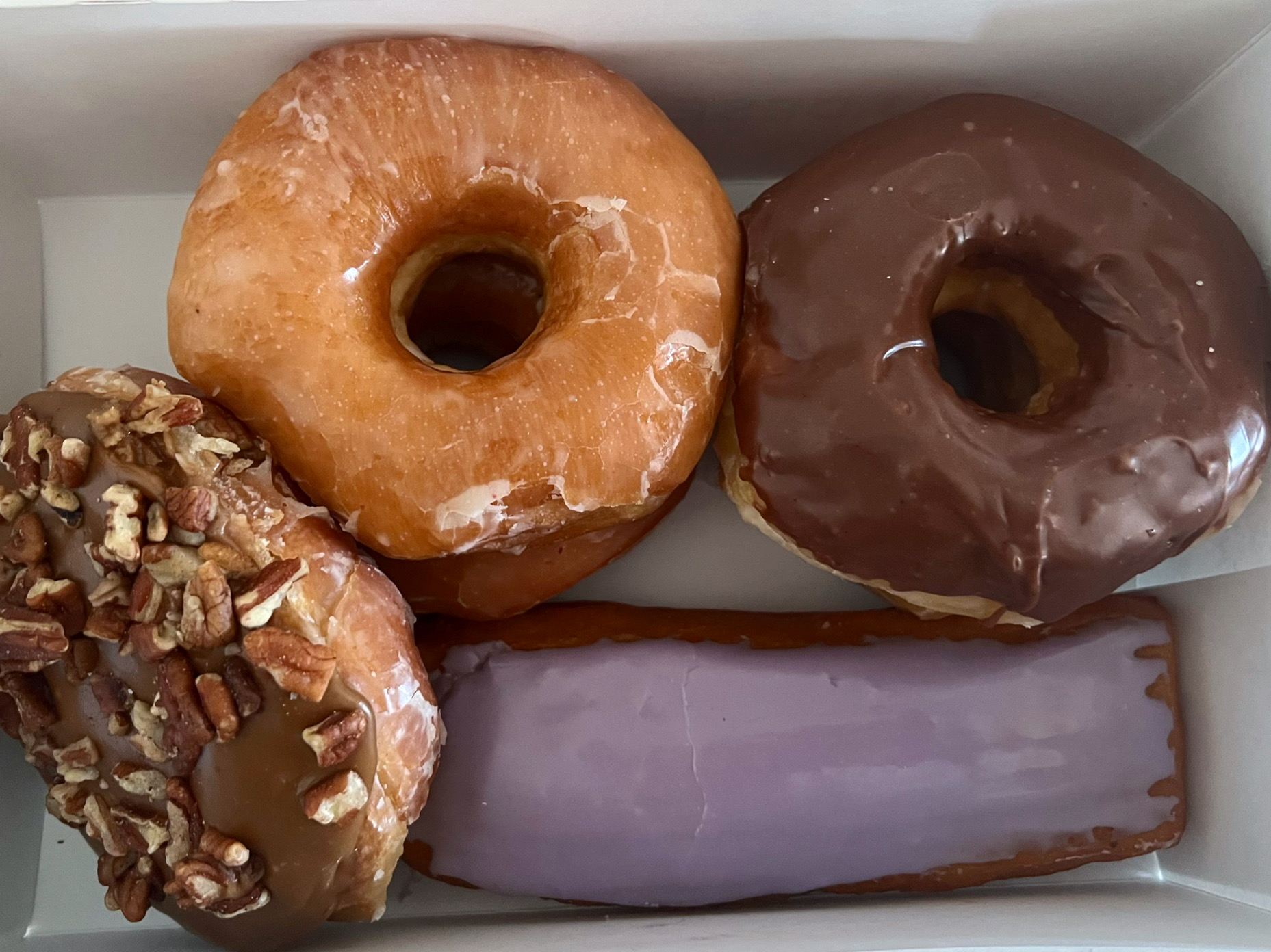 In a white box, there are assorted donuts of glazed, chocolate frosted, and a donut with chopped walnuts. Photo by Alyssa Buckley.