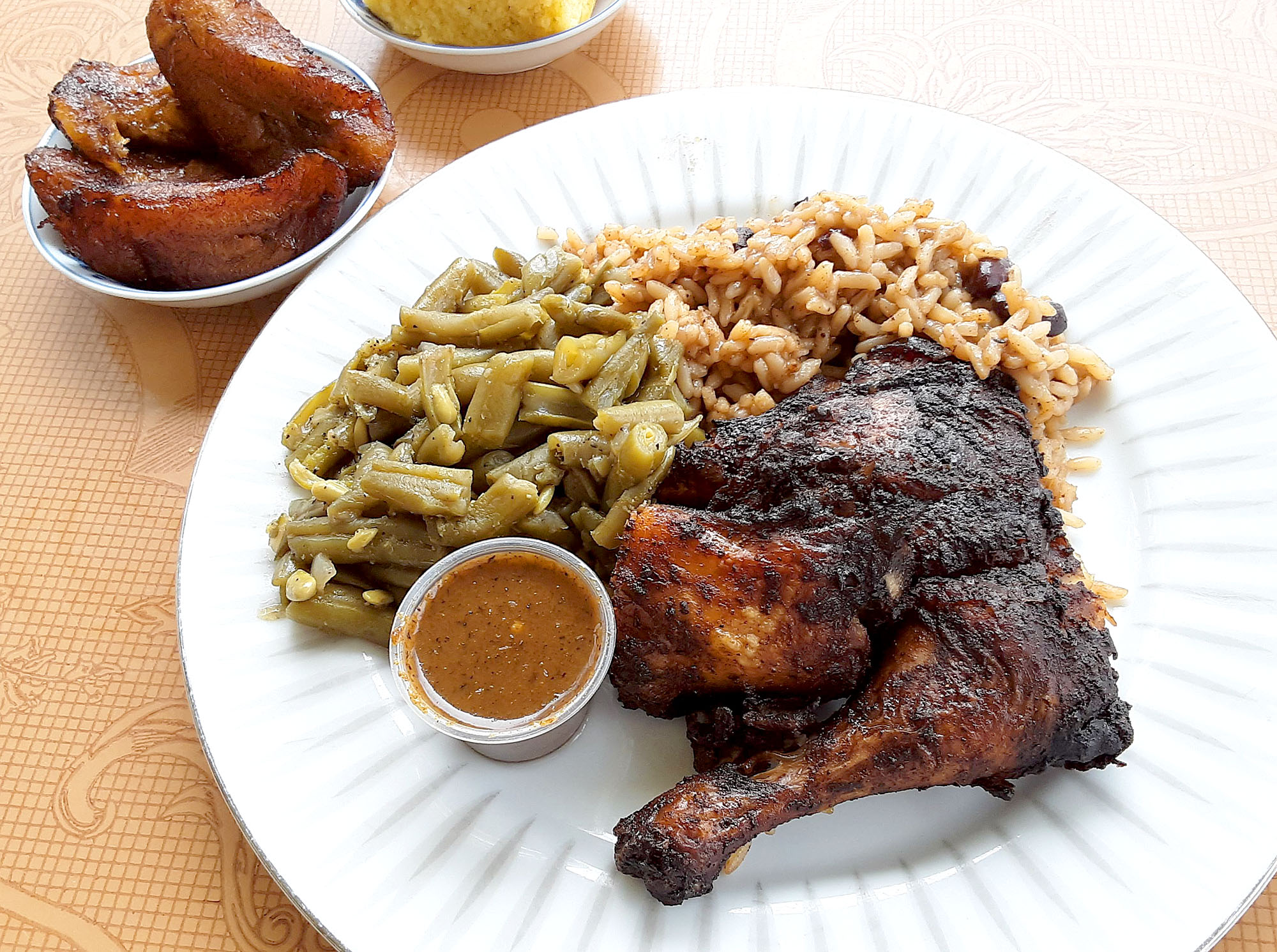 On a white plate, there is jerk chicken with the bone in, green beans, and a little bit of rice. Photo by Paul Young.