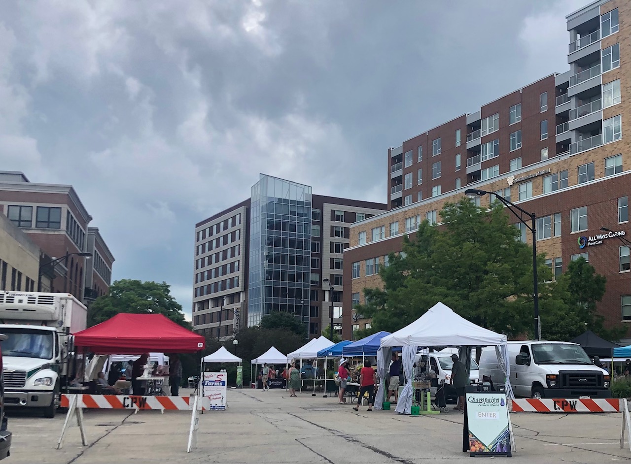 With a blue sky above, there is the Champaign farmers' market with tents set up with vendors.  Photo by Alyssa Buckley.