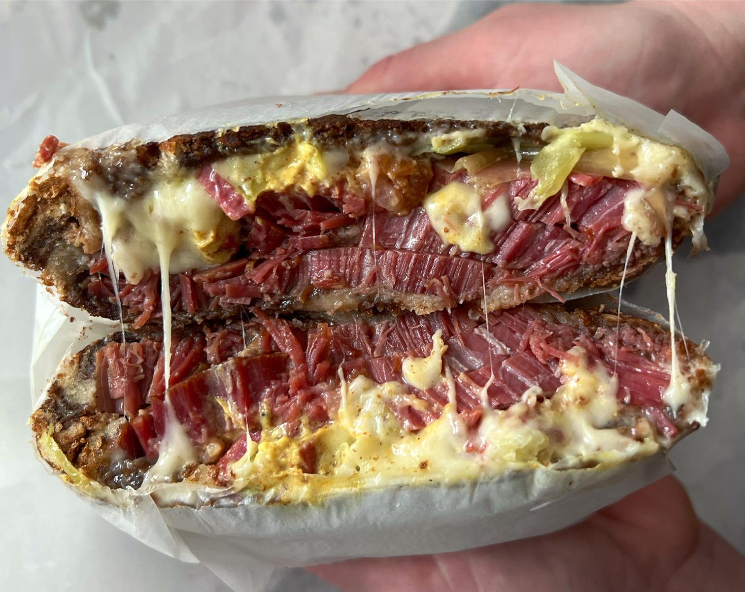 Two white hands hold a sliced pastrami sandwich from Baldarotta's. The baby Swiss cheese strings across red pastrami. Photo by Alyssa Buckley.
