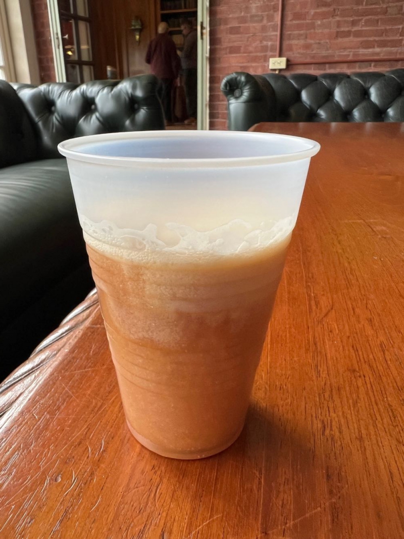 A clear plastic cup is three quarters of the way filled with brown liquid mixed with white frothy cream. Photo by Julie McClure.