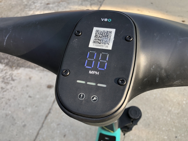 A close up photo of a speedometer in the center of the scooter's handlebars. There is a QR code at the top of the panel. Photo by Andrea Black.