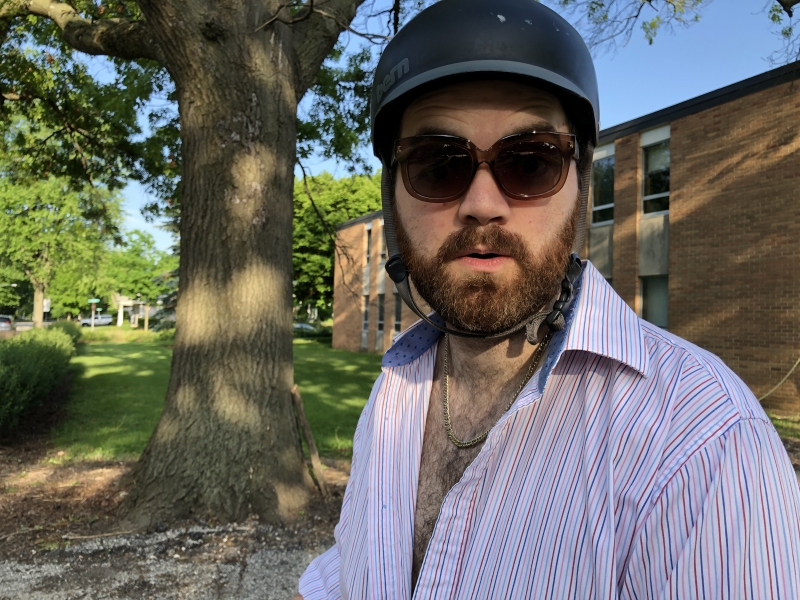 The writer wearing his helmet, round sunglasses, and a white striped collared shirt partially unbuttoned. He is staring at the camera. Photo by Andrea Black.