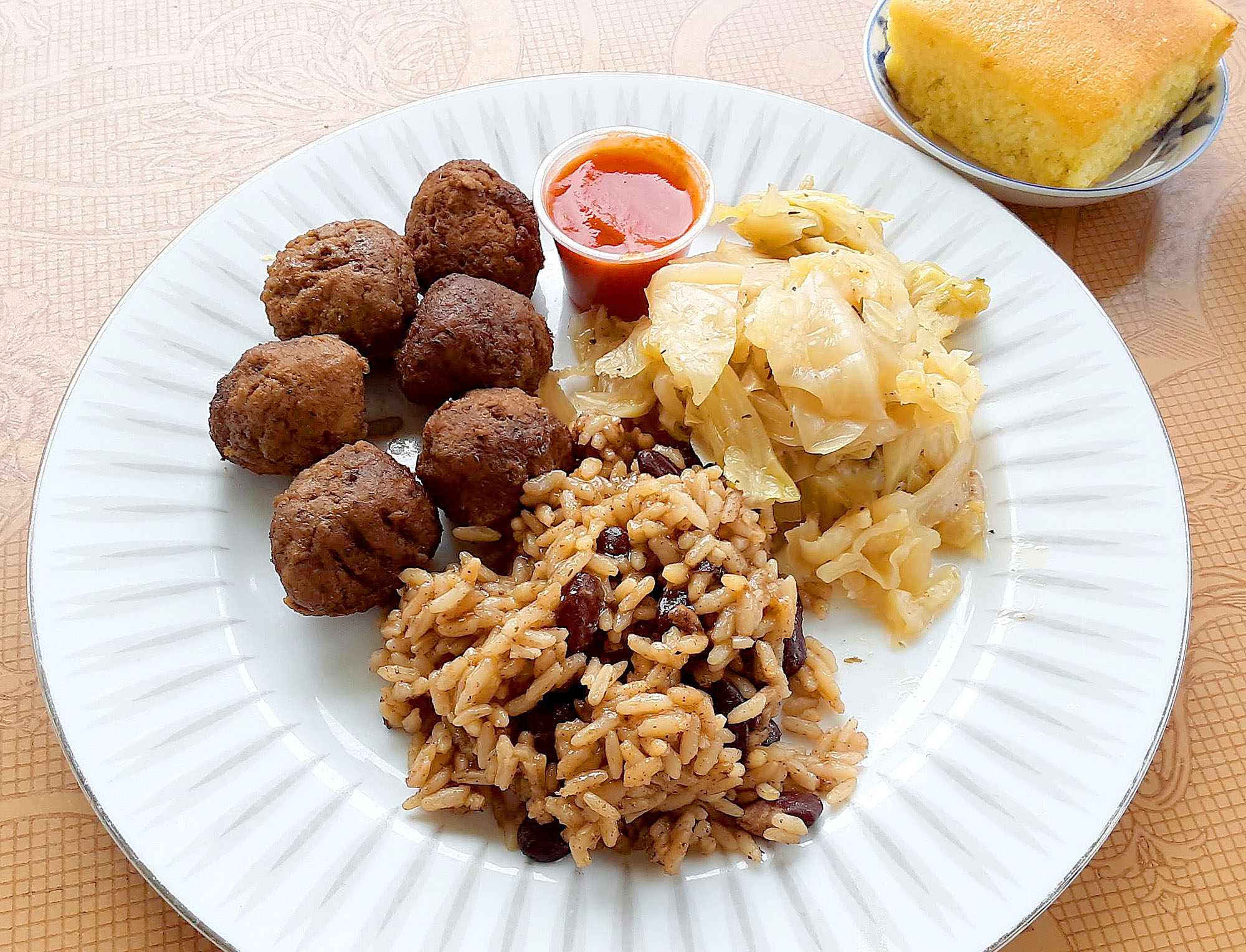 On a white plate, there are beef balls with a tiny cup and a side of rice with beans and cabbage. Photo by Paul Young.