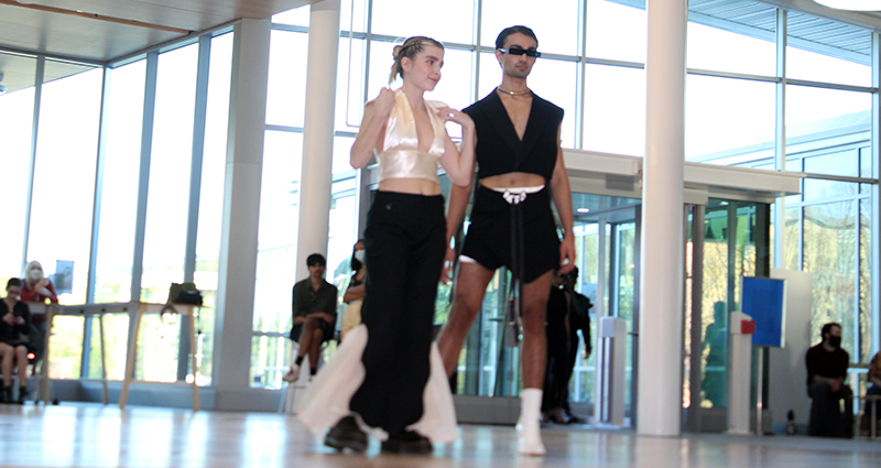 Female model in silver halter with black trousers and male model in black crop top and matching shorts.