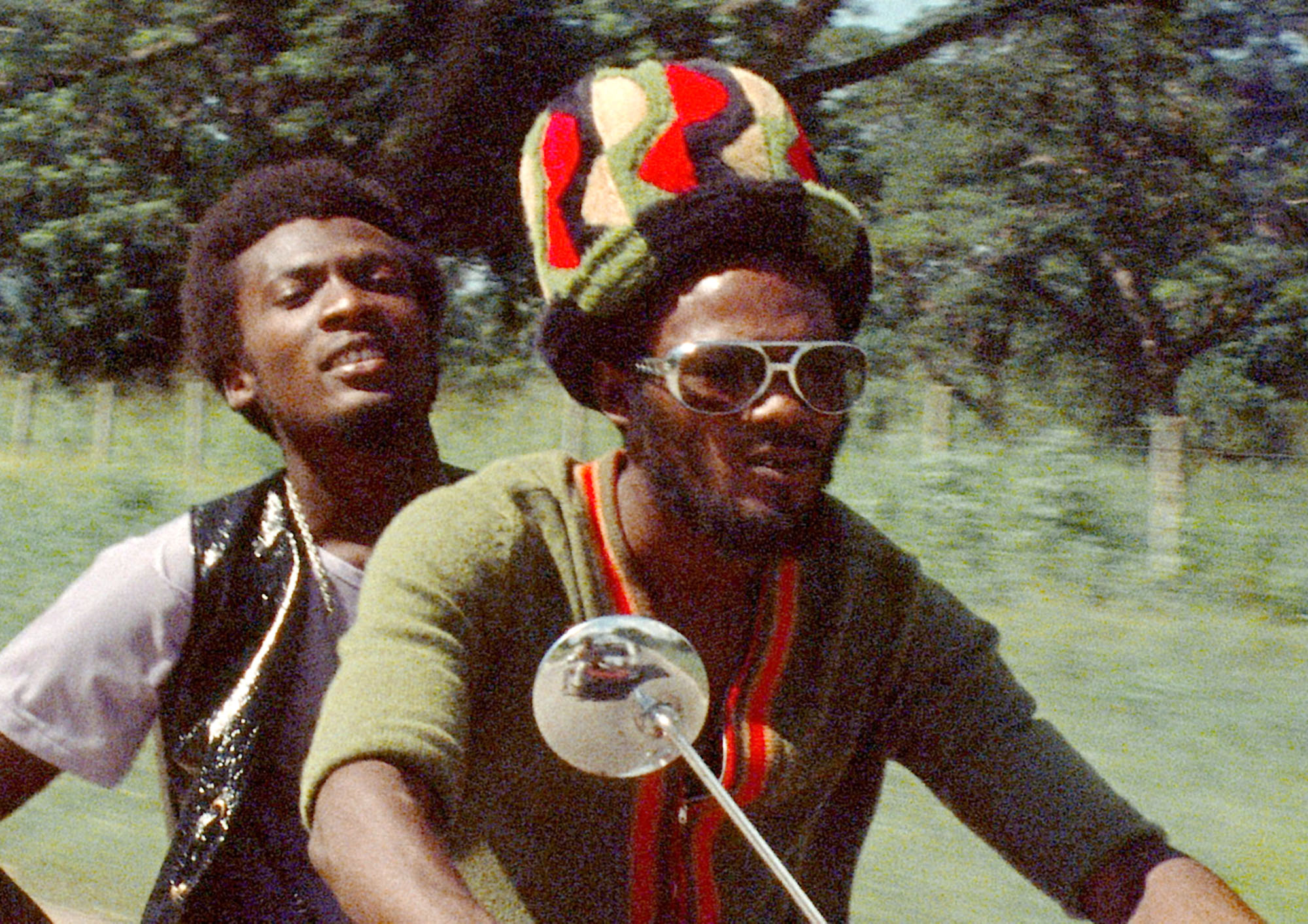 Two Jamaican men are on a motorcycle on a sunny day from the film The Harder They Come. Photo by New World Pictures.