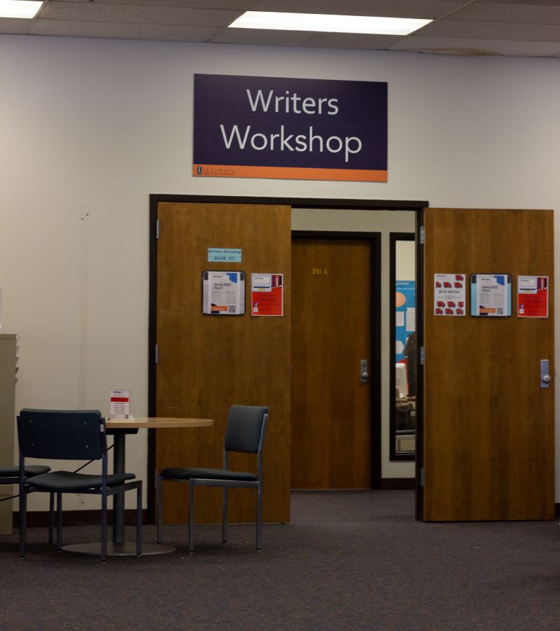 A doorway with brown wooden doors and a sign above the door that says Writer's Workshop. Photo by Jorge Murga.
