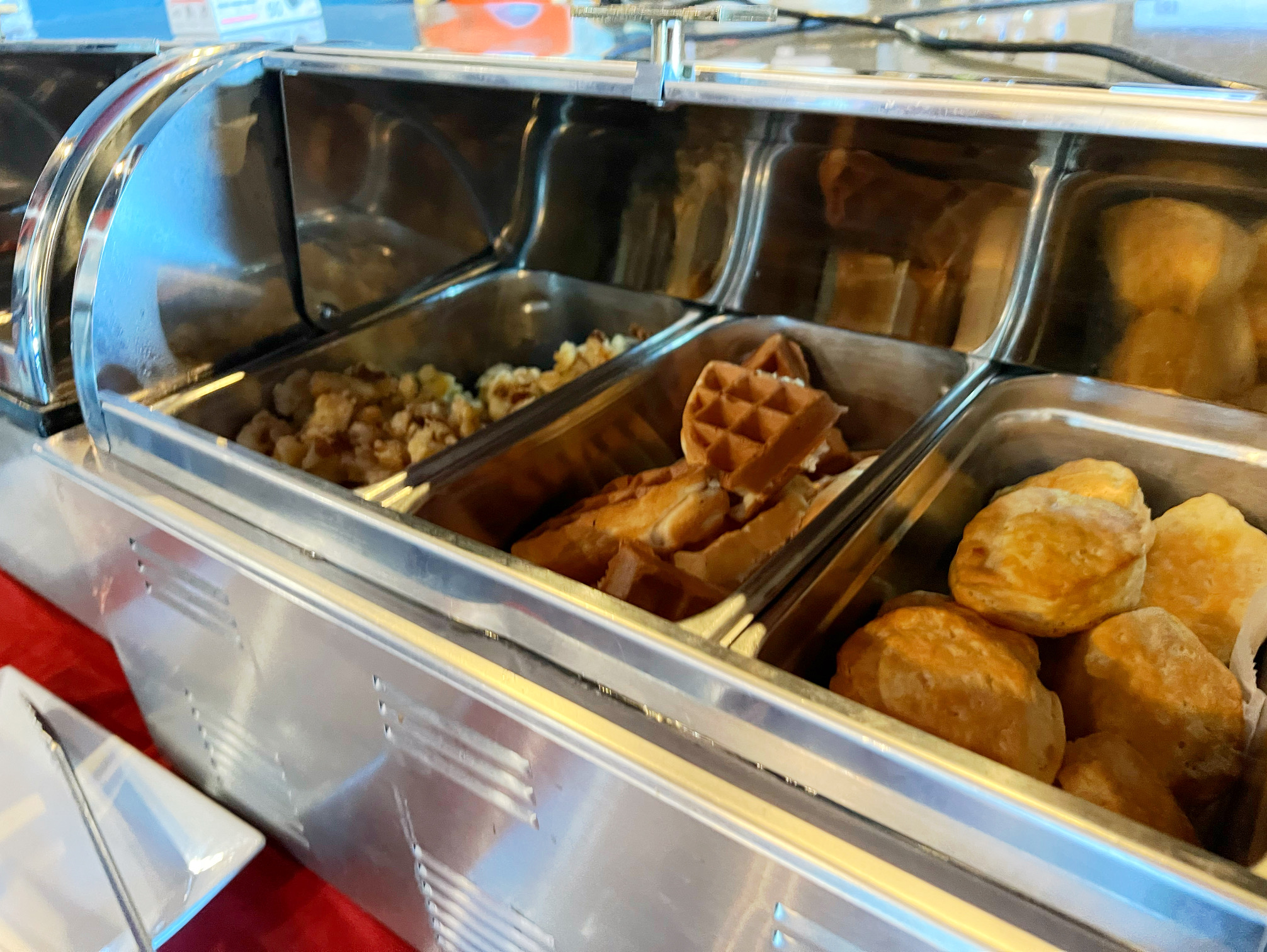 On the buffet, there is a silver metal container with three dividers holding breakfast potatoes, waffle triangles, and biscuits. Photo by Alyssa Buckley.