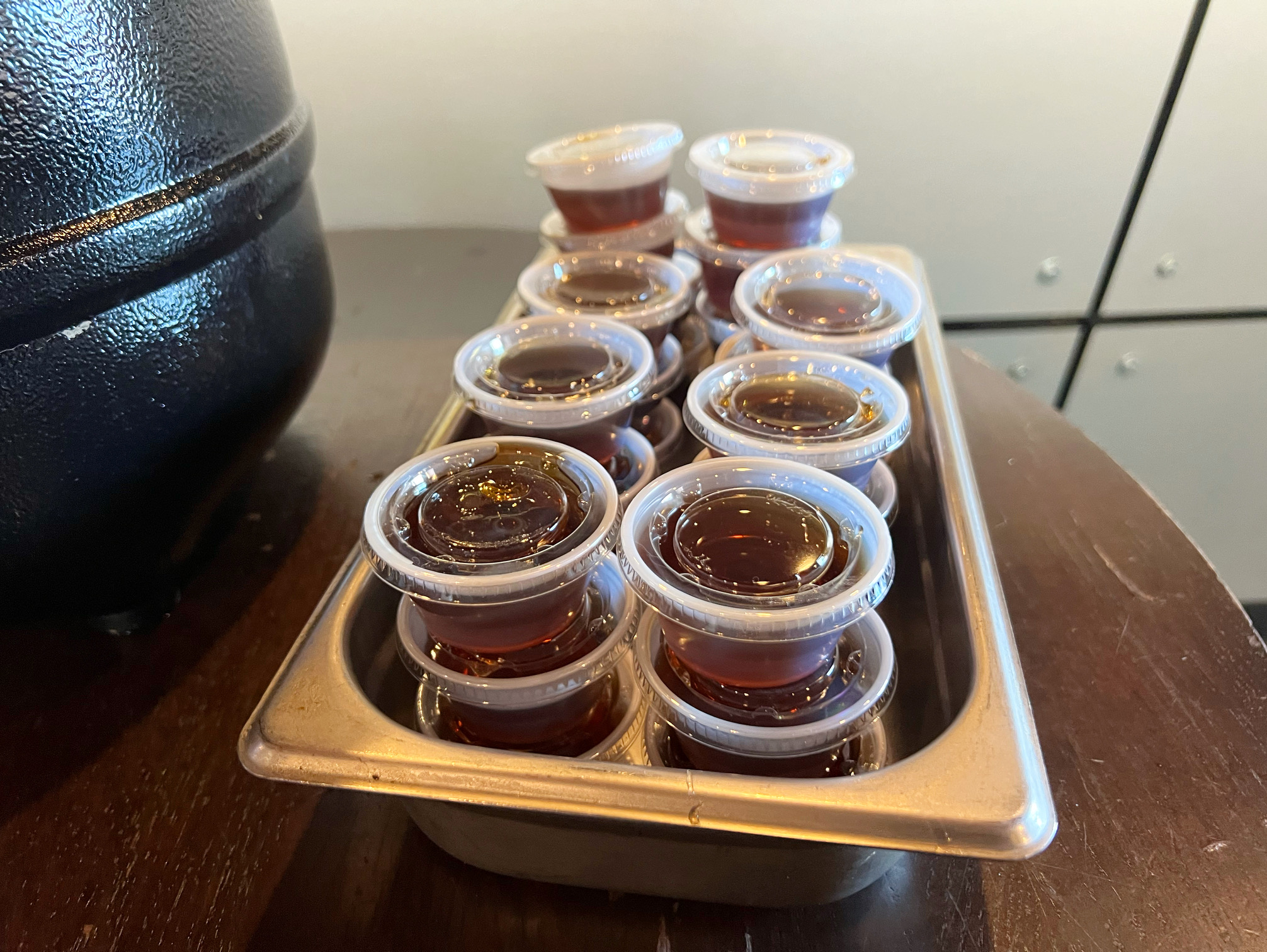 On a wooden table, there is a metal tray holding plastic individually sized cups of syrup. Photo by Alyssa Buckley.