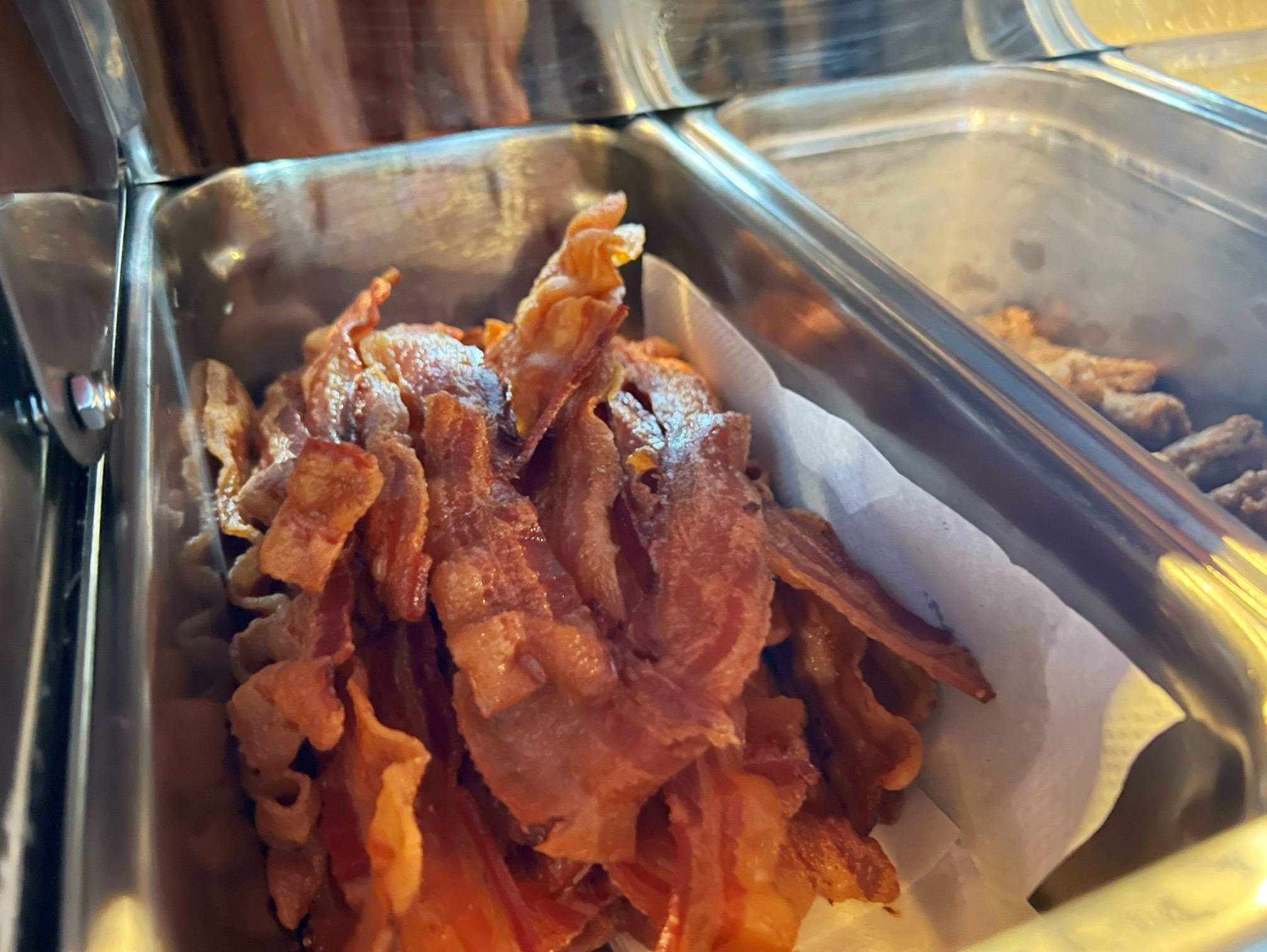 In a paper towel lined metal container, there are strips of bacon. Photo by Alyssa Buckley.